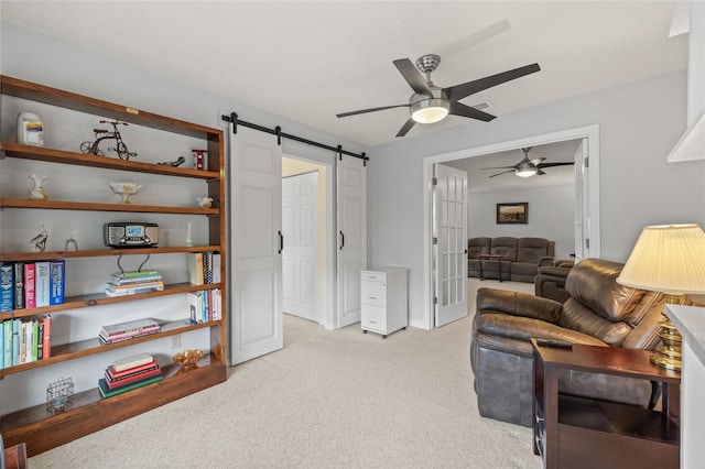 living area with a barn door, light carpet, and a ceiling fan