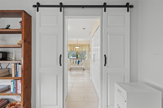 hall with a barn door, light tile patterned flooring, and visible vents