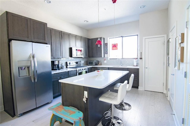 kitchen with light wood-style flooring, a breakfast bar area, stainless steel appliances, light countertops, and a sink