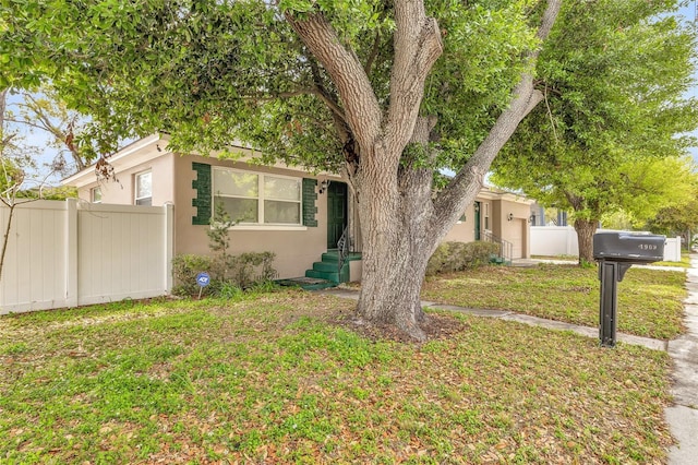 view of front facade with stucco siding, a front lawn, and fence