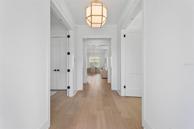 hall featuring a chandelier, light wood finished floors, and baseboards