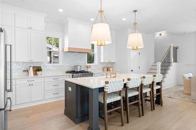 kitchen with custom range hood, backsplash, light wood-style floors, stainless steel fridge, and range