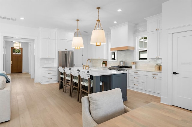 kitchen featuring light countertops, visible vents, freestanding refrigerator, premium range hood, and a kitchen breakfast bar