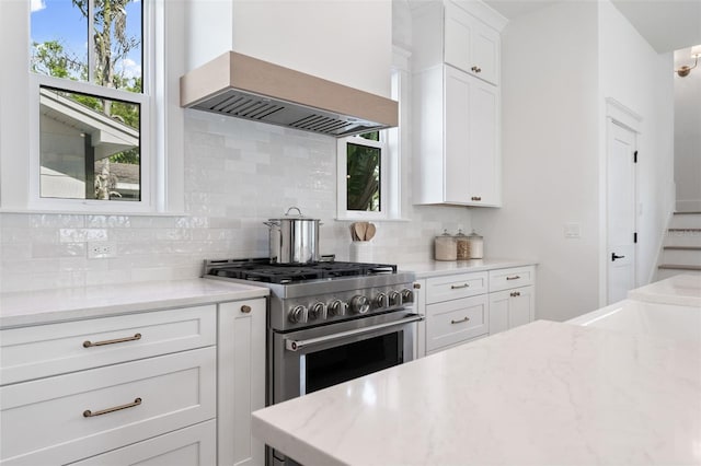 kitchen with premium range hood, white cabinets, backsplash, high end range, and light stone countertops