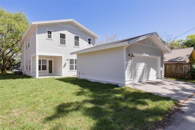 back of house with a garage, an outbuilding, fence, decorative driveway, and a yard