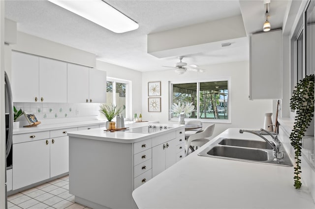 kitchen with black electric cooktop, a sink, a ceiling fan, light countertops, and tasteful backsplash