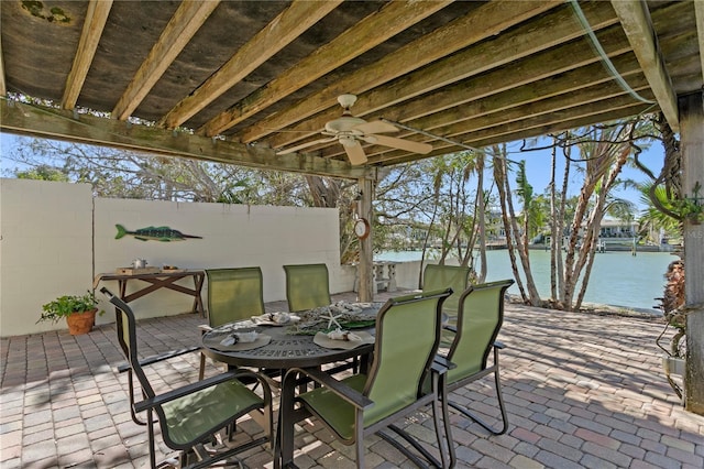 view of patio with a ceiling fan, outdoor dining area, a water view, and fence