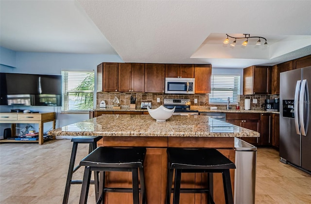 kitchen featuring stainless steel appliances, backsplash, a raised ceiling, and light stone countertops