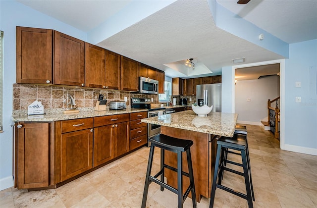 kitchen featuring light stone counters, stainless steel appliances, a breakfast bar, decorative backsplash, and a center island