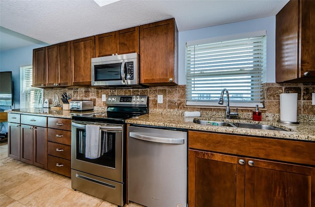 kitchen featuring appliances with stainless steel finishes, a sink, backsplash, and light stone counters