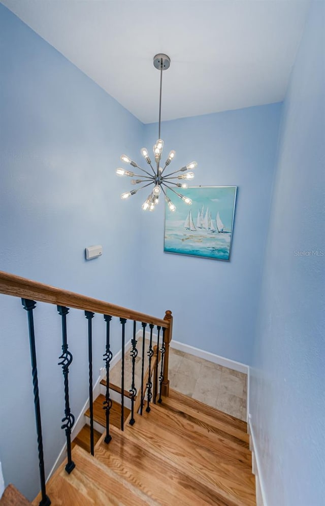 staircase with a chandelier, wood finished floors, and baseboards