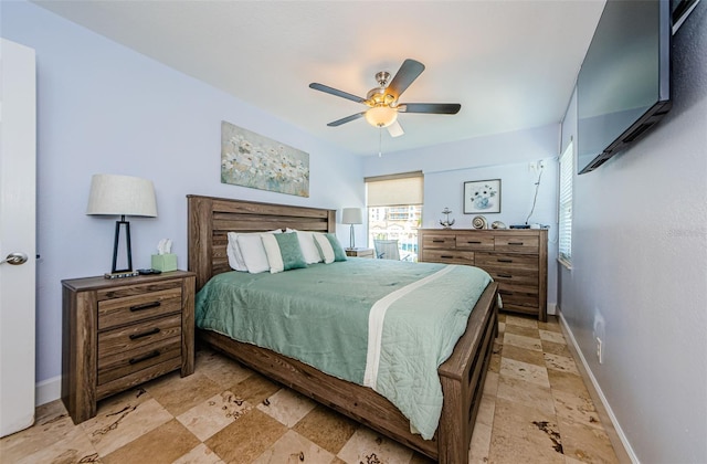 bedroom with stone tile floors, baseboards, and ceiling fan