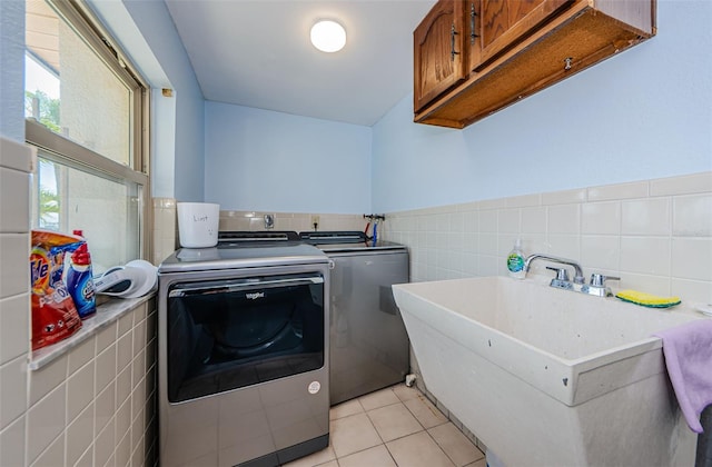 laundry area featuring cabinet space, light tile patterned floors, a sink, washing machine and dryer, and tile walls