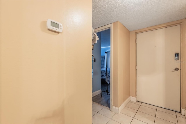 corridor with baseboards, a textured ceiling, and light tile patterned flooring