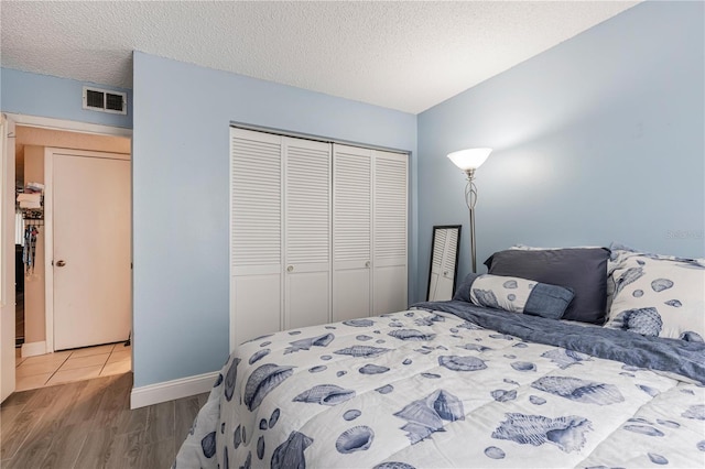 bedroom featuring wood finished floors, baseboards, visible vents, a closet, and a textured ceiling