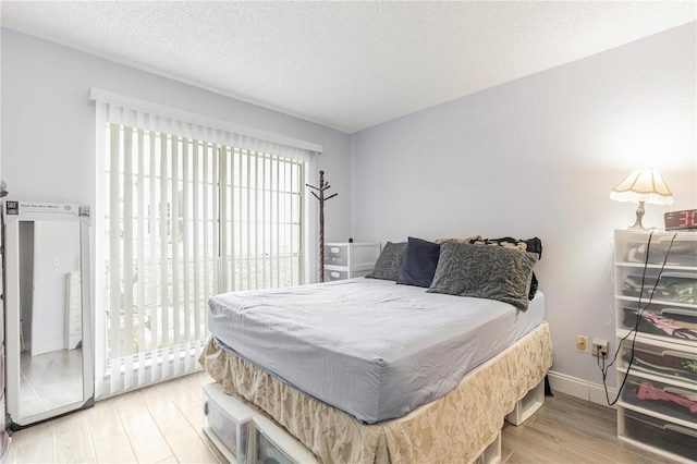 bedroom featuring access to exterior, a textured ceiling, baseboards, and wood finished floors