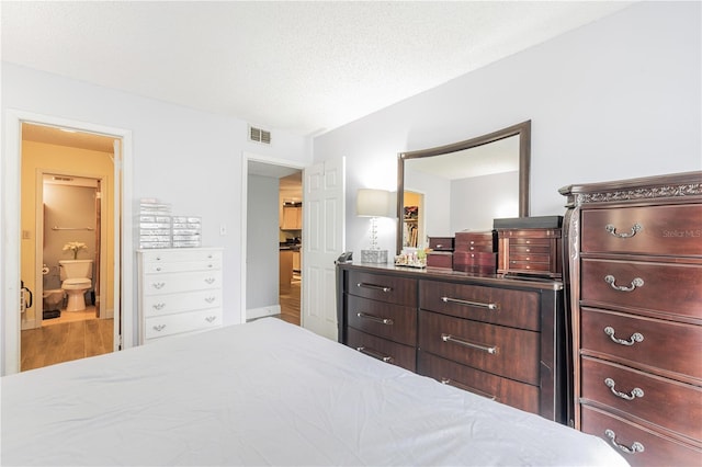 bedroom featuring visible vents, ensuite bathroom, and wood finished floors