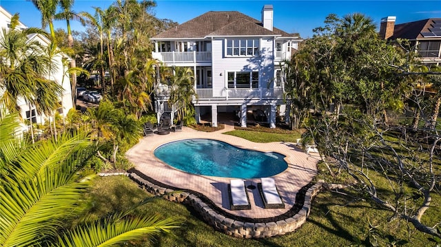 rear view of property with a balcony, an outdoor pool, a chimney, stairs, and a patio area