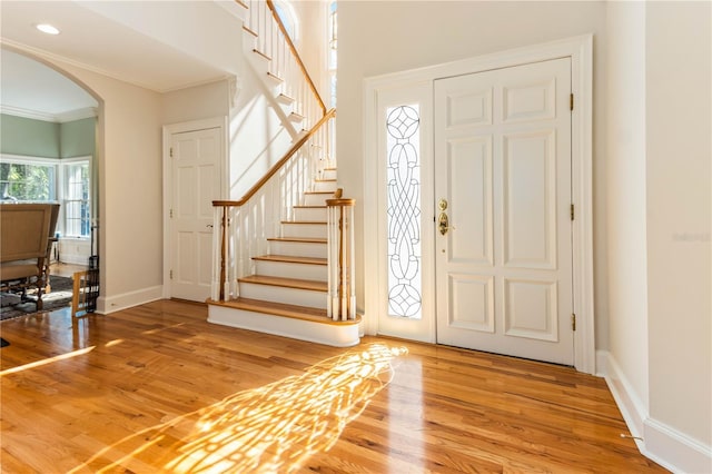 entryway with baseboards, stairway, ornamental molding, wood finished floors, and arched walkways