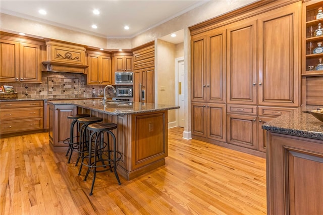 kitchen with a kitchen bar, light wood-style flooring, a sink, stainless steel microwave, and brown cabinetry