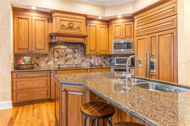 kitchen with a sink, stainless steel microwave, tasteful backsplash, and brown cabinetry