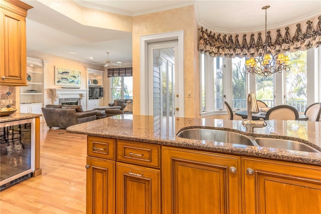 kitchen featuring a fireplace, a sink, wine cooler, crown molding, and a notable chandelier