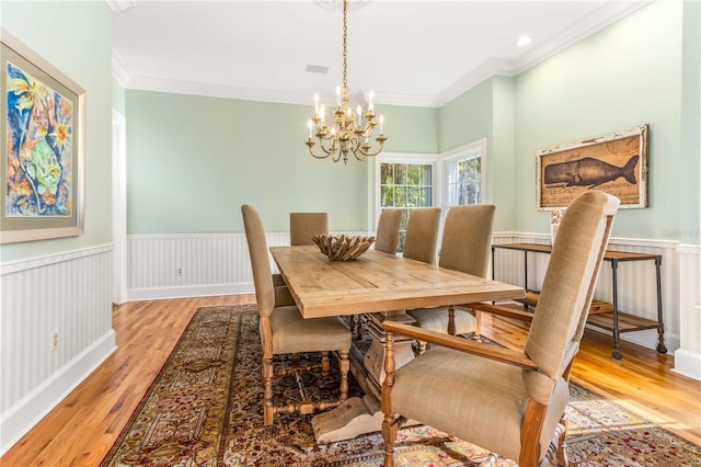 dining space with light wood finished floors, a wainscoted wall, a chandelier, and ornamental molding