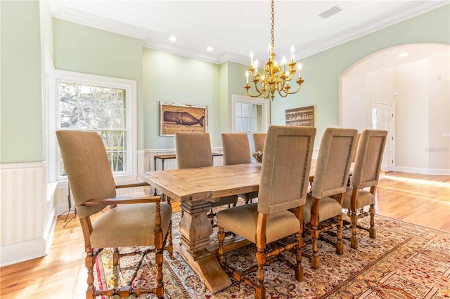 dining space featuring ornamental molding, arched walkways, an inviting chandelier, wainscoting, and light wood finished floors