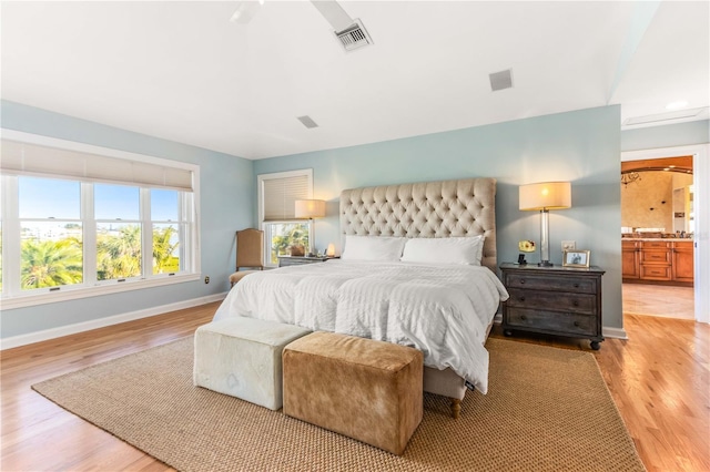 bedroom featuring connected bathroom, visible vents, baseboards, and wood finished floors