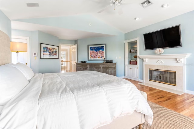 bedroom with light wood finished floors, visible vents, a high end fireplace, and vaulted ceiling