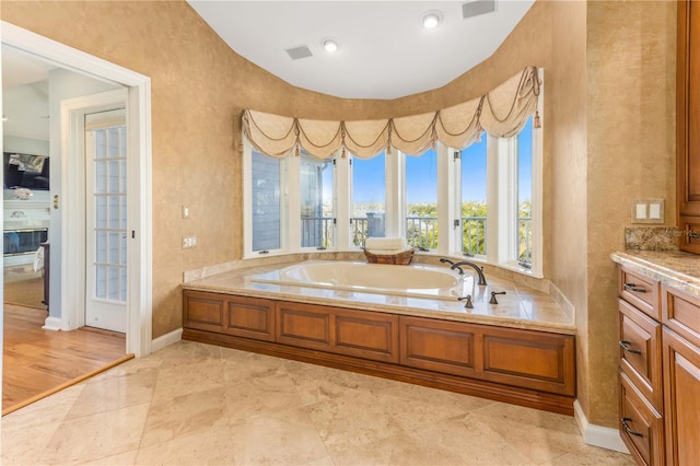 full bathroom featuring visible vents, a garden tub, a glass covered fireplace, baseboards, and vanity