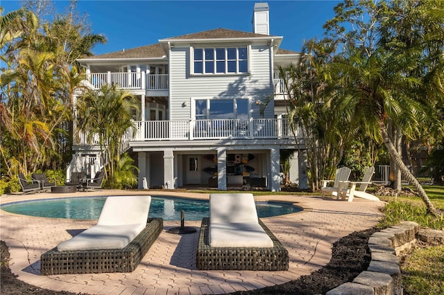 rear view of house featuring stairway, a balcony, an outdoor pool, a chimney, and a patio area