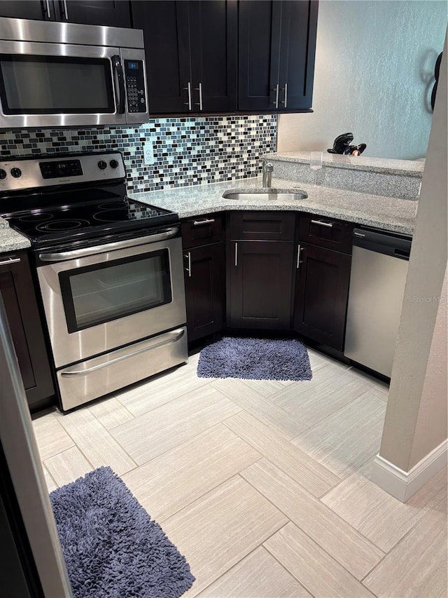 kitchen with appliances with stainless steel finishes, dark cabinetry, a sink, and decorative backsplash