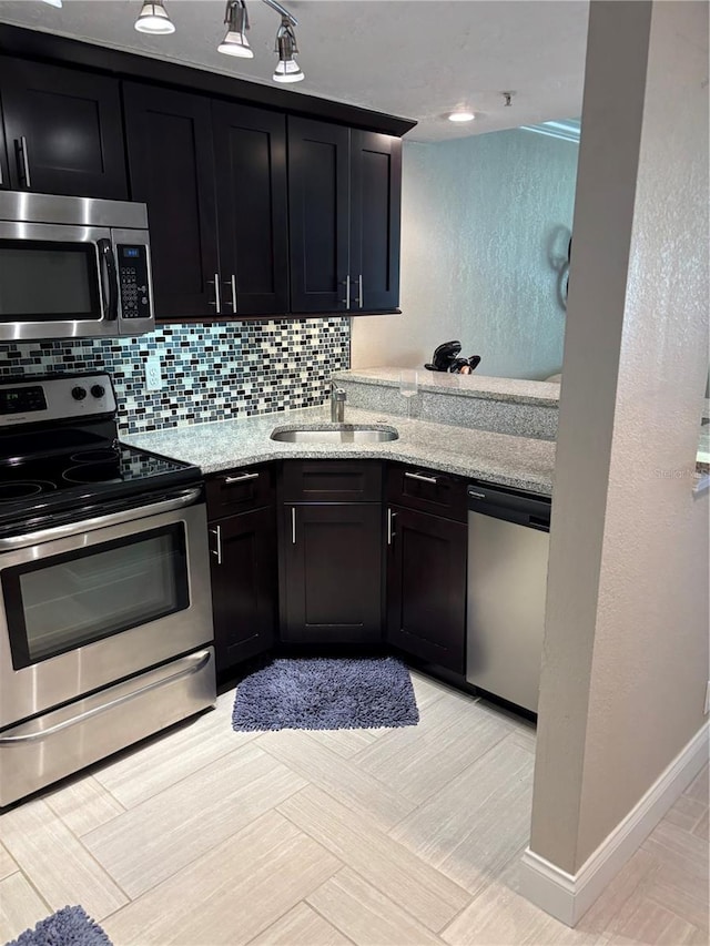 kitchen featuring stainless steel appliances, dark cabinetry, a sink, and decorative backsplash