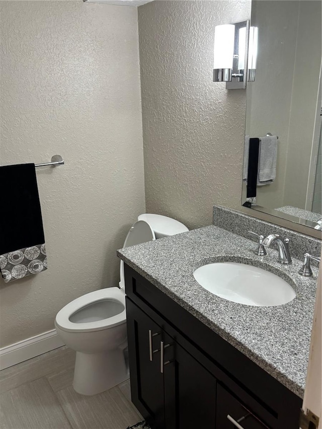 bathroom featuring toilet, vanity, and a textured wall