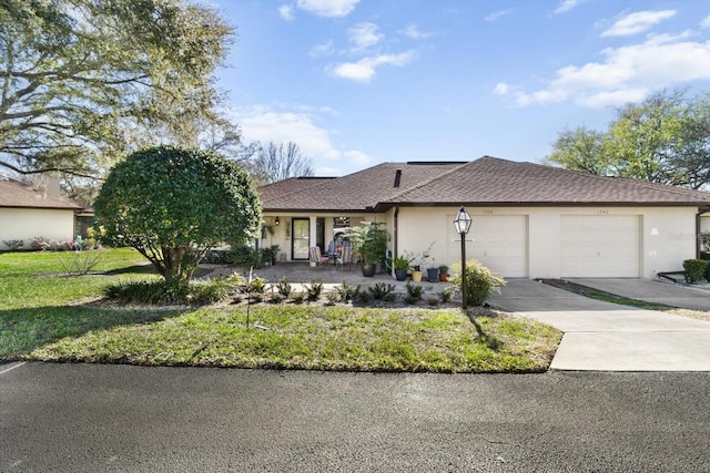 ranch-style home featuring an attached garage, concrete driveway, roof with shingles, stucco siding, and a front lawn