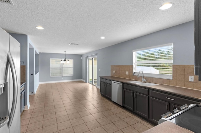 kitchen featuring a notable chandelier, a sink, stainless steel appliances, light tile patterned floors, and decorative backsplash