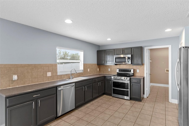 kitchen with light tile patterned floors, a sink, decorative backsplash, appliances with stainless steel finishes, and dark countertops