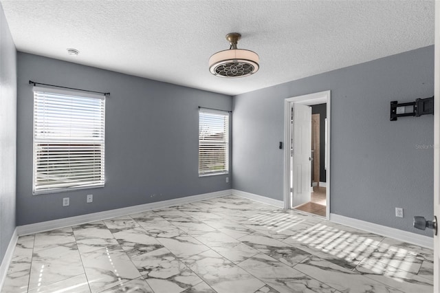 spare room featuring baseboards, marble finish floor, and a textured ceiling