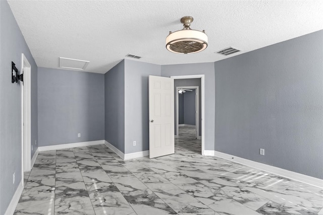 spare room with visible vents, a textured ceiling, attic access, and baseboards