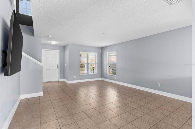 empty room featuring light tile patterned floors, baseboards, and a textured ceiling