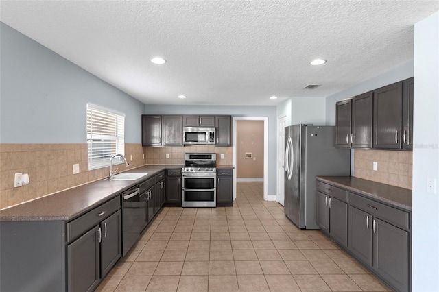 kitchen with a sink, dark countertops, light tile patterned flooring, and stainless steel appliances