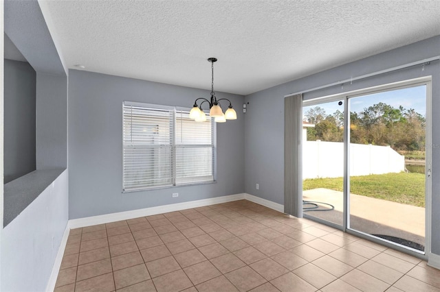 empty room featuring a chandelier, tile patterned floors, a textured ceiling, and baseboards