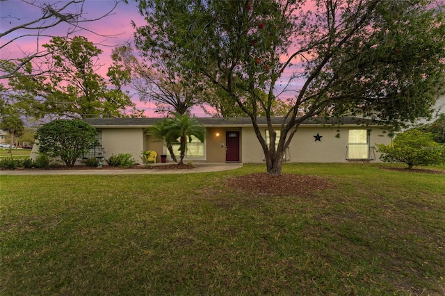 ranch-style home featuring a lawn and stucco siding