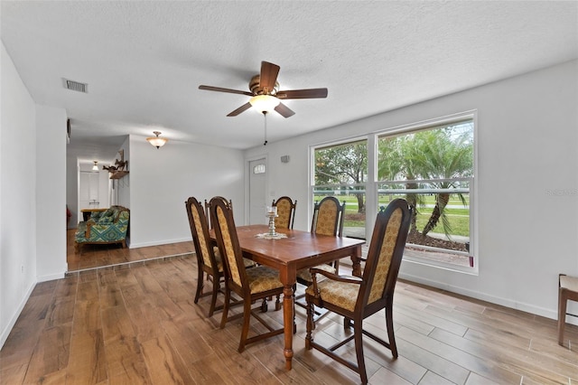 dining room with a textured ceiling, wood finished floors, visible vents, and baseboards