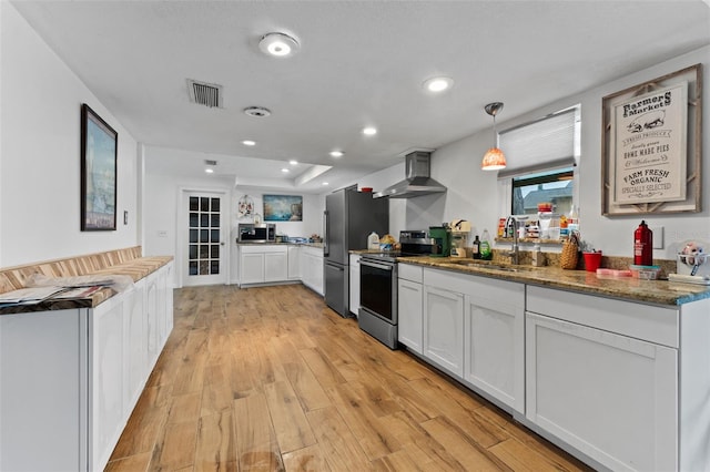 kitchen featuring visible vents, appliances with stainless steel finishes, light wood-style floors, a sink, and wall chimney range hood