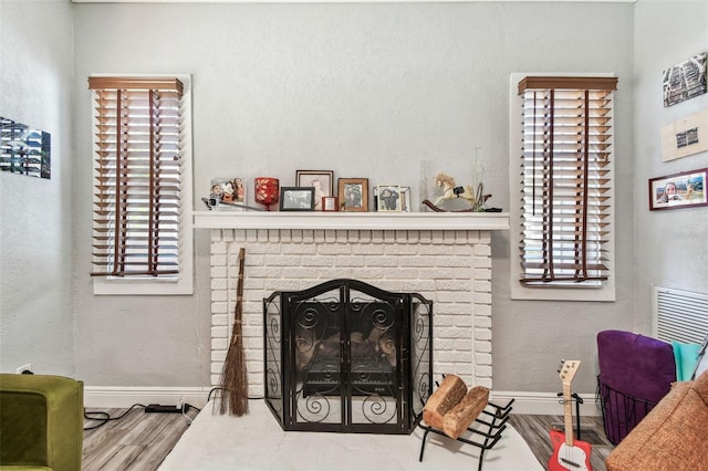 living room featuring a brick fireplace, wood finished floors, baseboards, and a textured wall