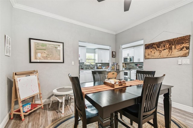 dining room featuring crown molding, a ceiling fan, light wood-type flooring, and baseboards