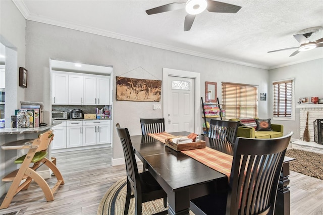 dining area featuring ceiling fan, a brick fireplace, light wood-style flooring, and crown molding