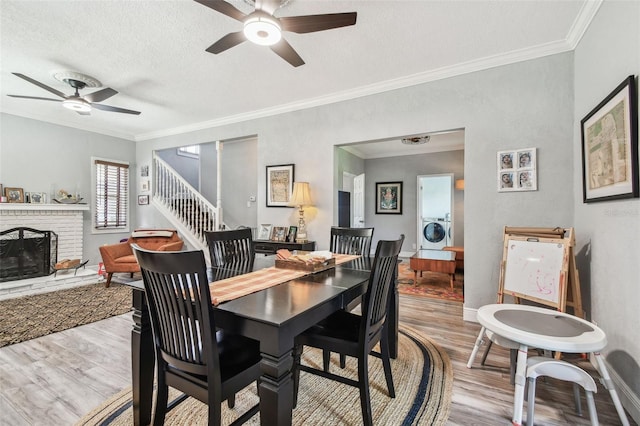 dining space with wood finished floors, washer / clothes dryer, ornamental molding, a textured ceiling, and a brick fireplace